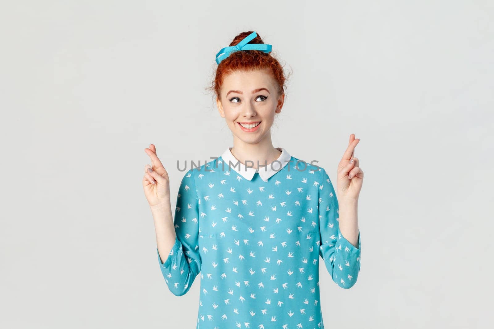 Smiling hopeful ginger woman with bun hairstyle, standing with crossed fingers, making wish. by Khosro1