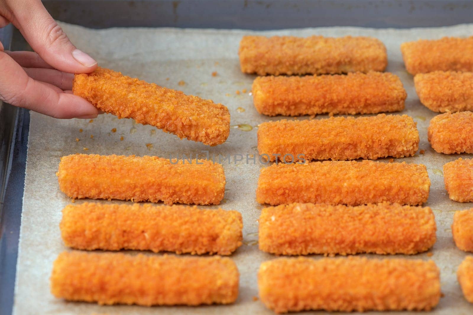 The hand lays out the fish fingers on the frying paper. The concept of frying fish sticks in the oven. Side view. High quality photo