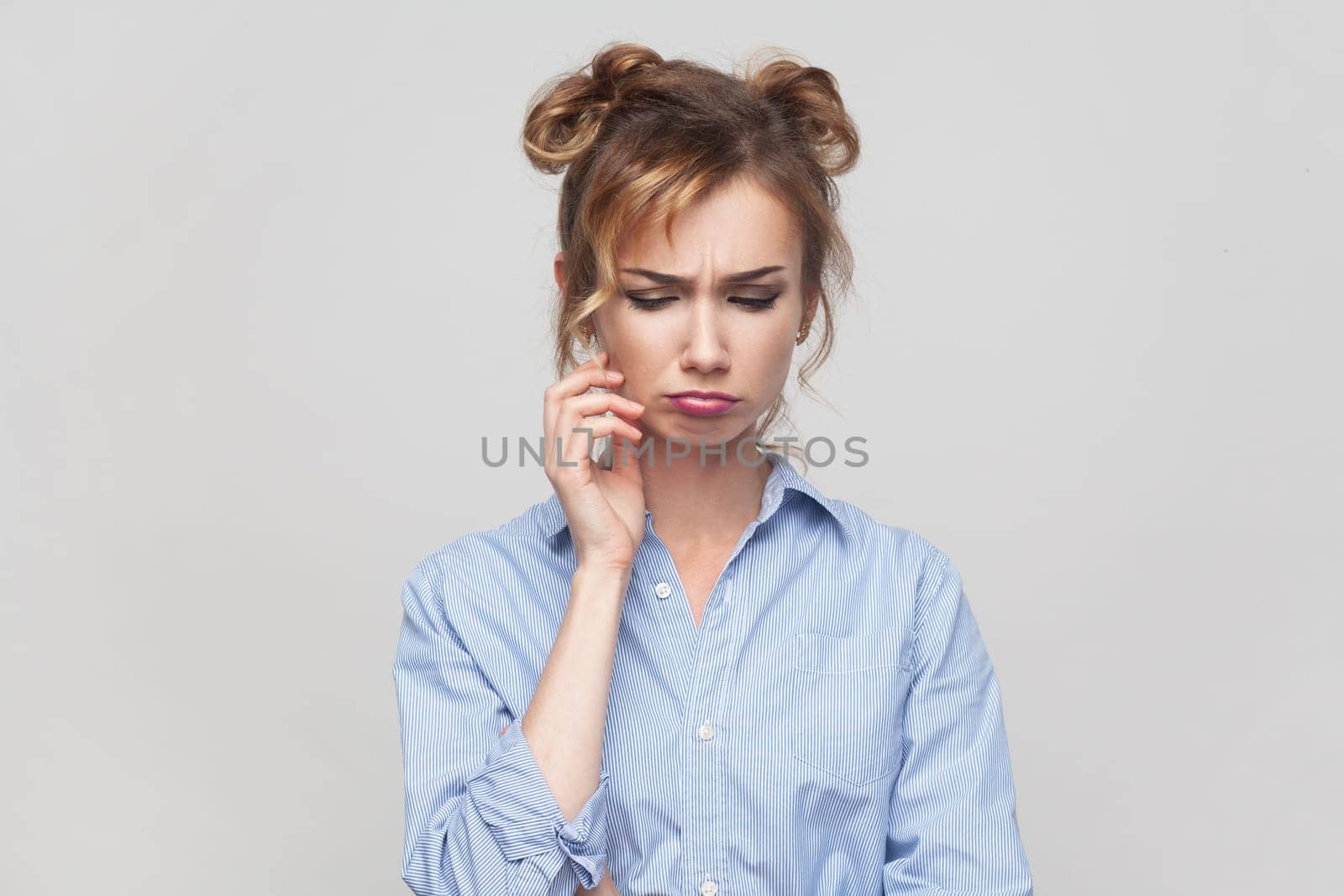 Portrait of sad blonde woman wearing blue shirt showing negative emotions upset because of bad news complains about unfair life. Indoor studio shot isolated on gray background.