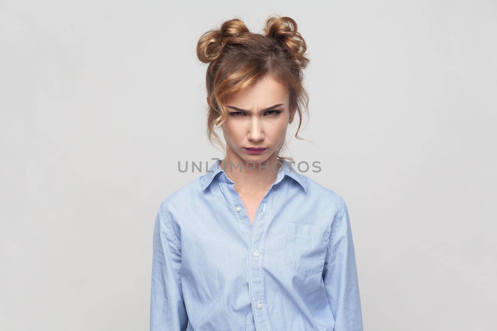 Portrait of annoyed irritated angry blonde woman feeling anxious and nervous, expressing fury and madness, wearing blue shirt. Indoor studio shot isolated on gray background.