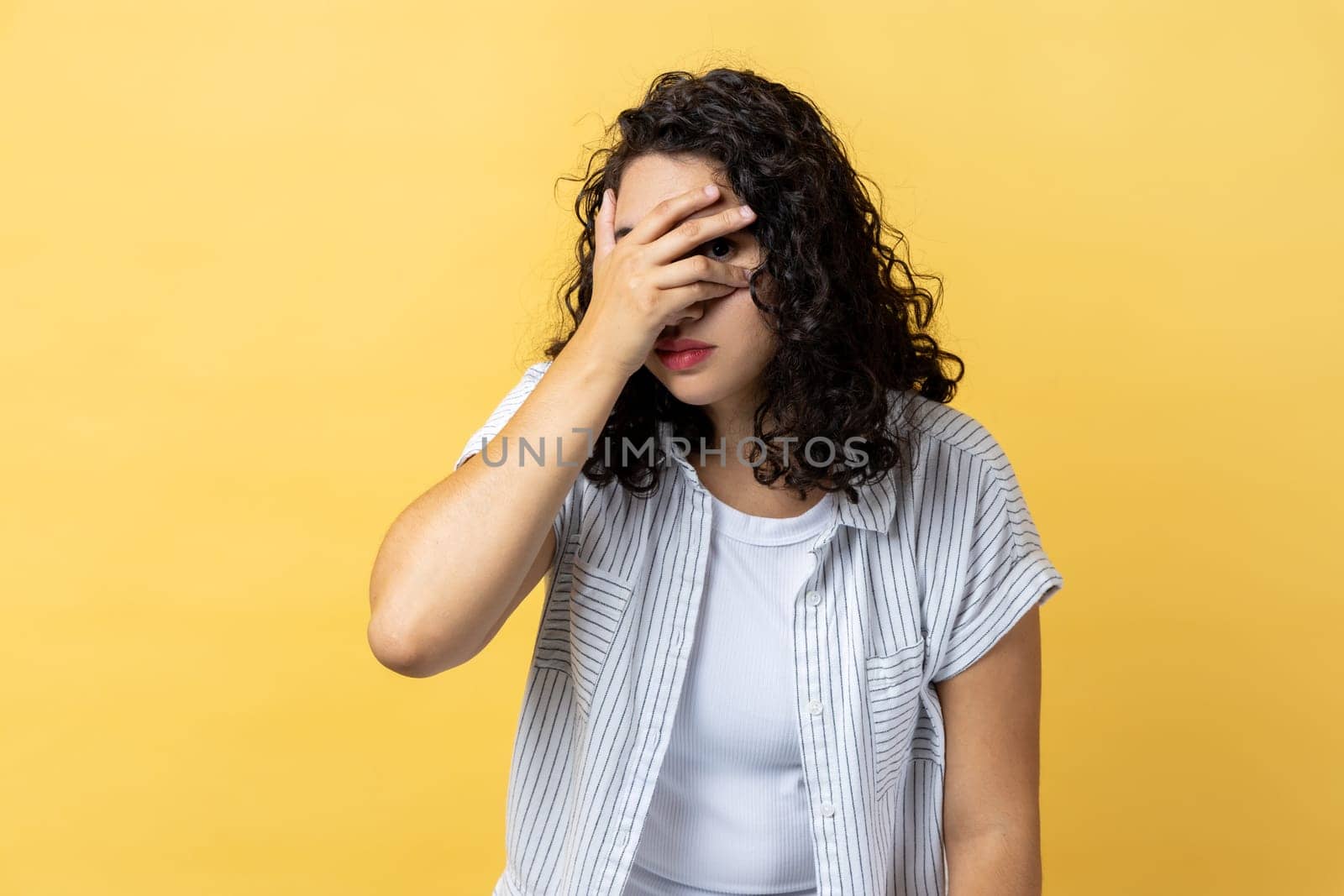 Woman spying through hole in fingers closing eyes with arm, peeking, sees something interesting. by Khosro1