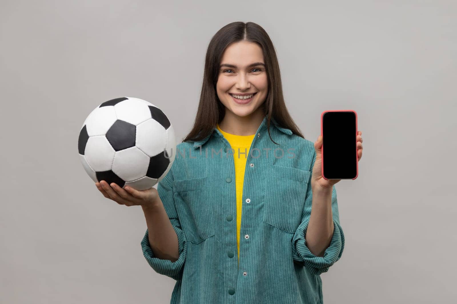 Woman with dark hair holding and showing blank display smartphone and football ball. by Khosro1