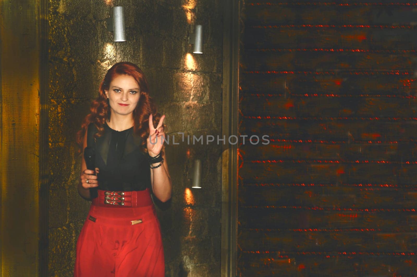 Red haired event host with a microphone in a room with lanterns and a red wall by jovani68