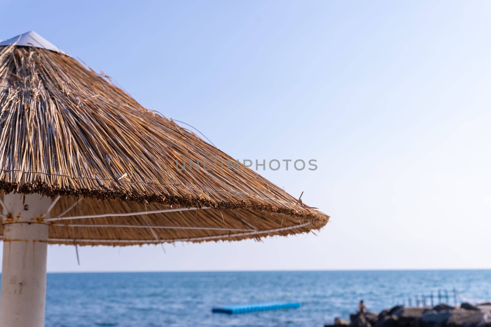Looking at the blue sea through a straw beach umbrella