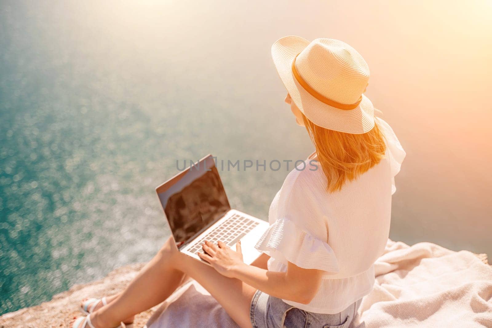 Freelance woman working on a laptop by the sea, typing away on the keyboard while enjoying the beautiful view, highlighting the idea of remote work