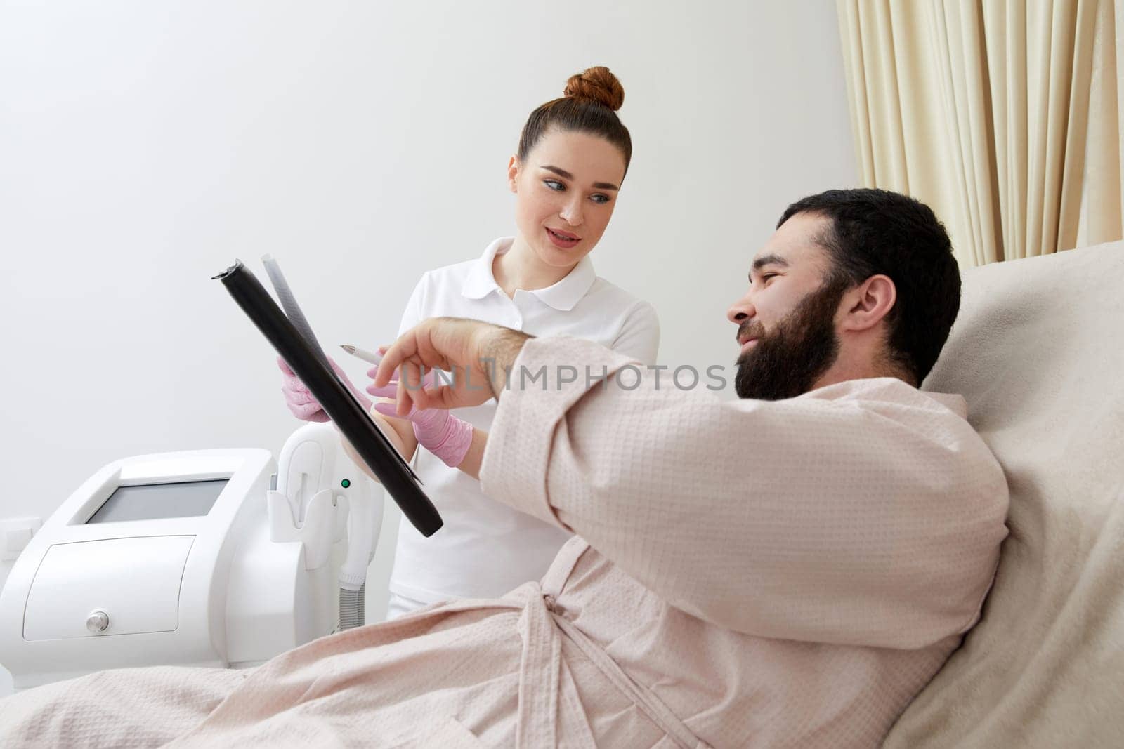 Smiling lady shows paper to man client sitting in comfortable armchair in cosmetological clinic