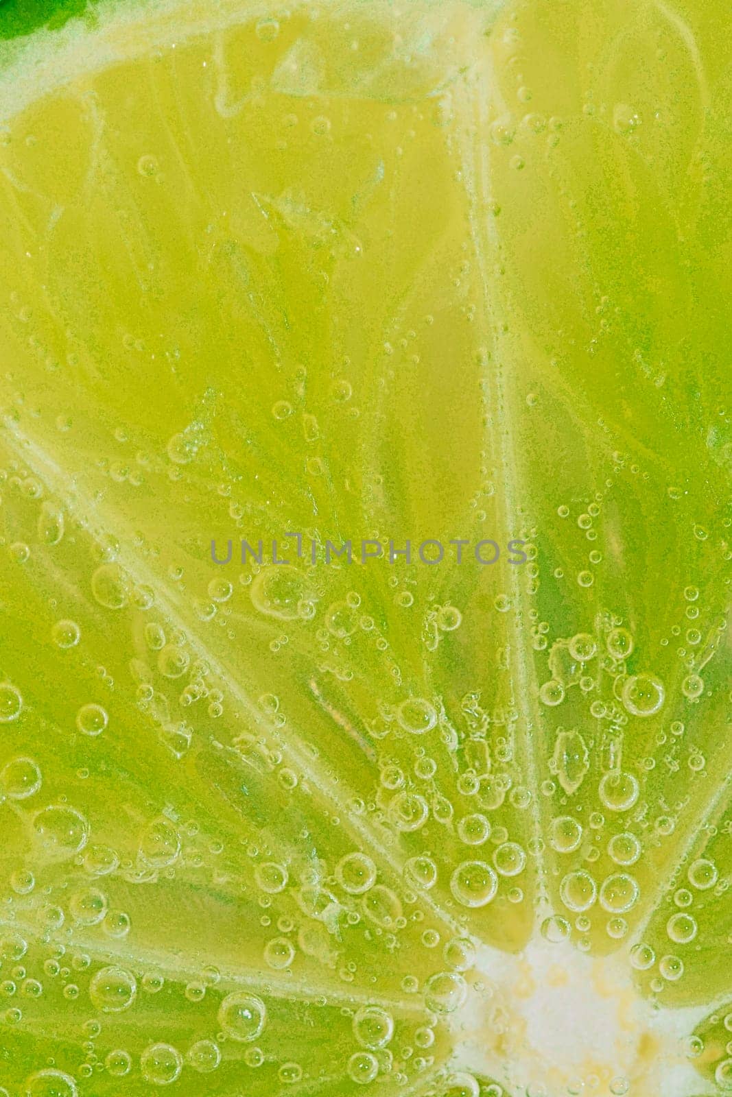 Close-up of a lime slice in liquid with bubbles. Slice of ripe lime in water. Close-up of fresh lime slice covered by bubbles. Macro vertical image