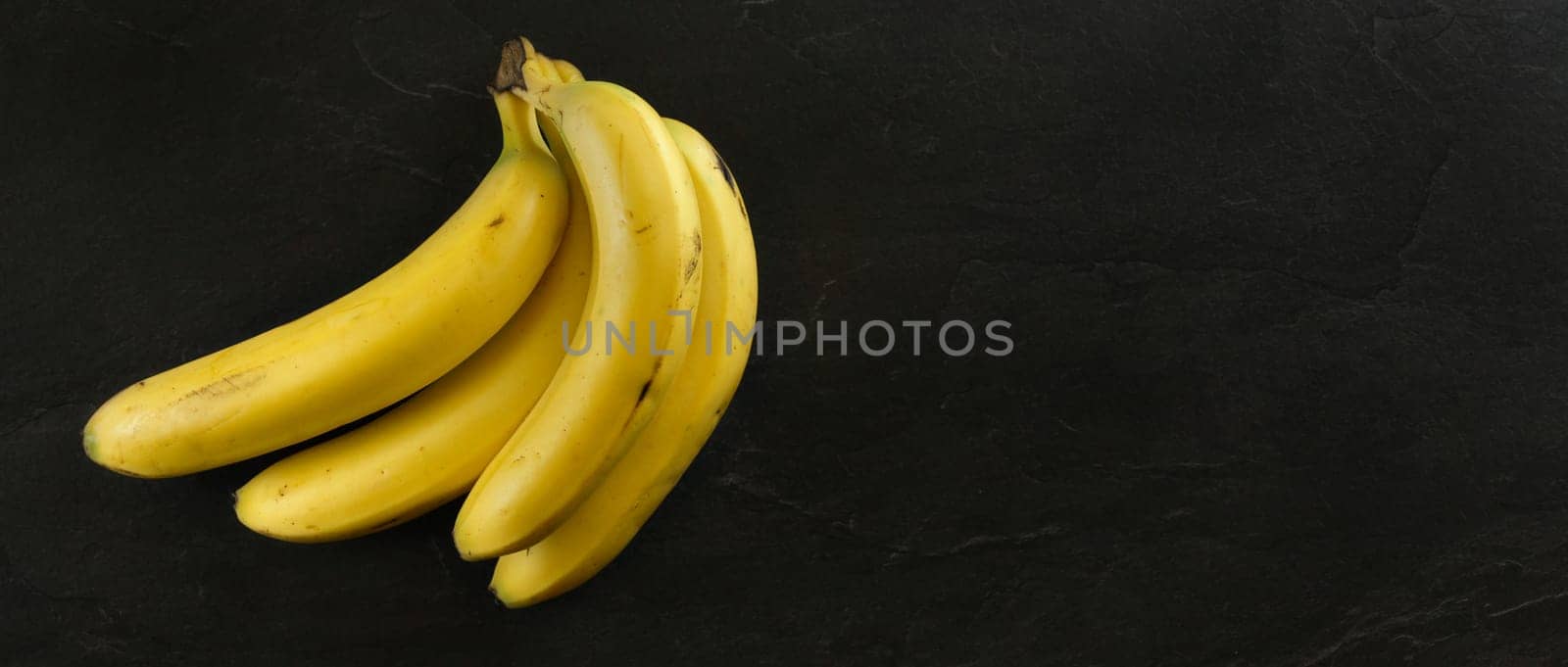 Top view, bunch of bananas on black stone board. Banner with copy space for text on right. by Ivanko