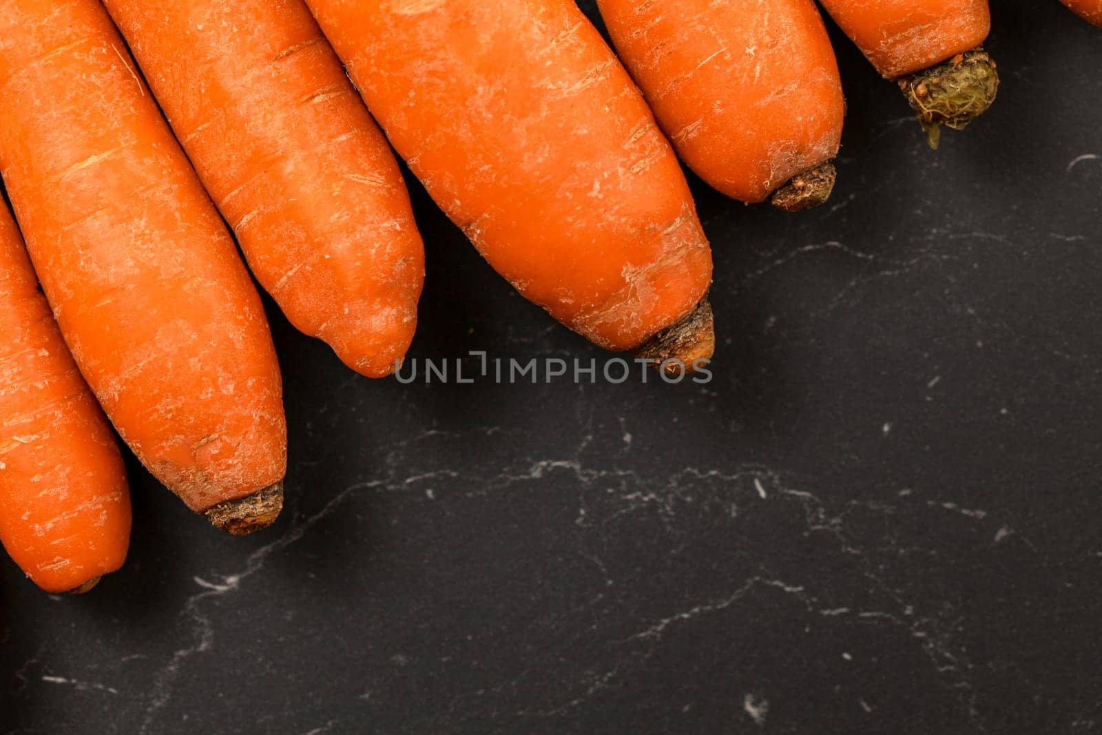 Top down view, detail of carrots on black board, space for text in down right corner.