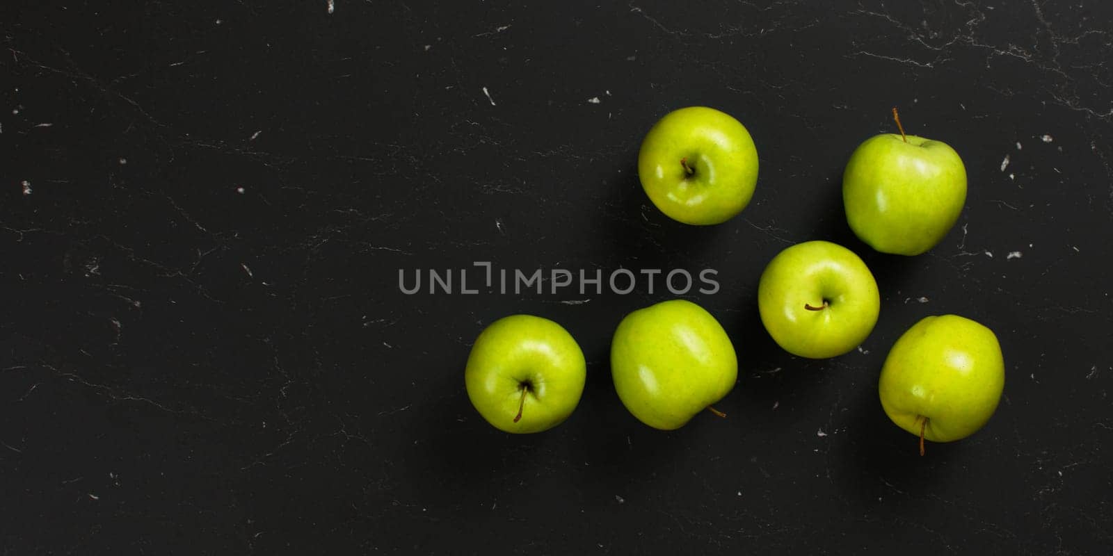 Top down view, six green apples on black marble board. Space for text left by Ivanko