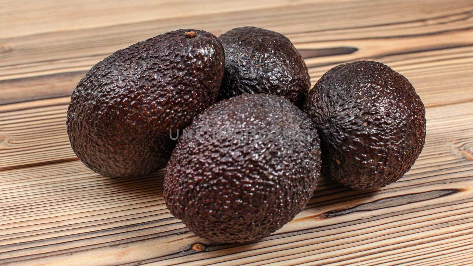 Four dark brown ripe avocados on wooden boards table.