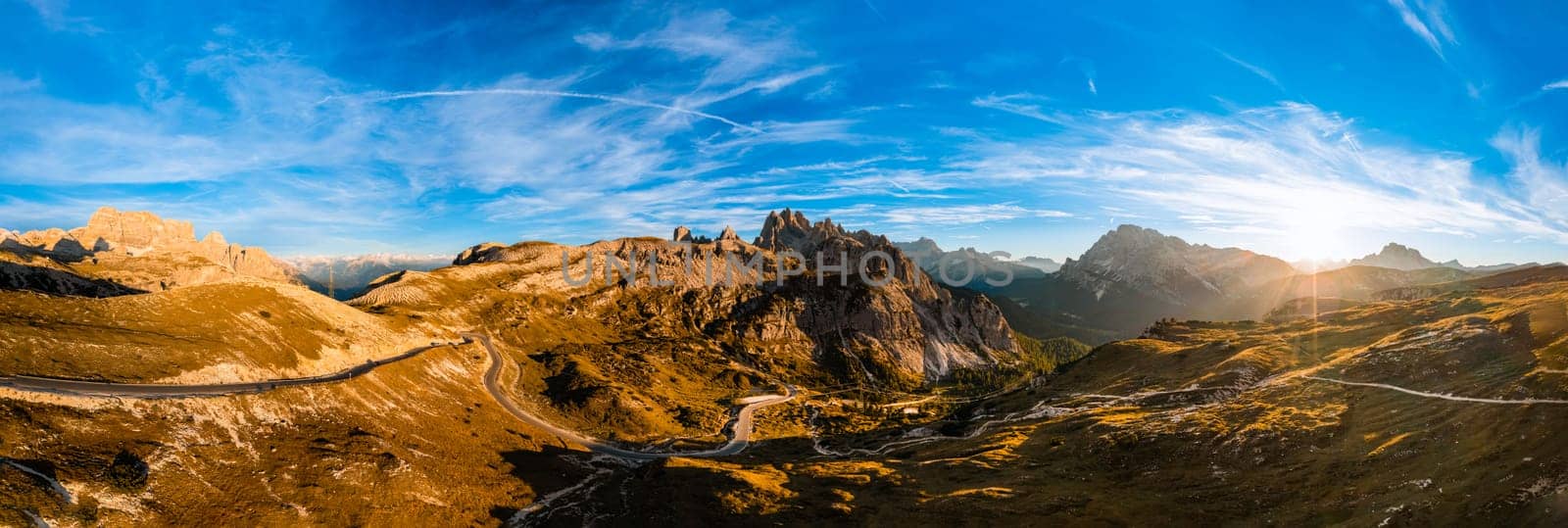 High stone columns of mountain massif of Tre Cime di Lavaredo at sunset. Battlement-like peaks under blue sky with white clouds aerial view