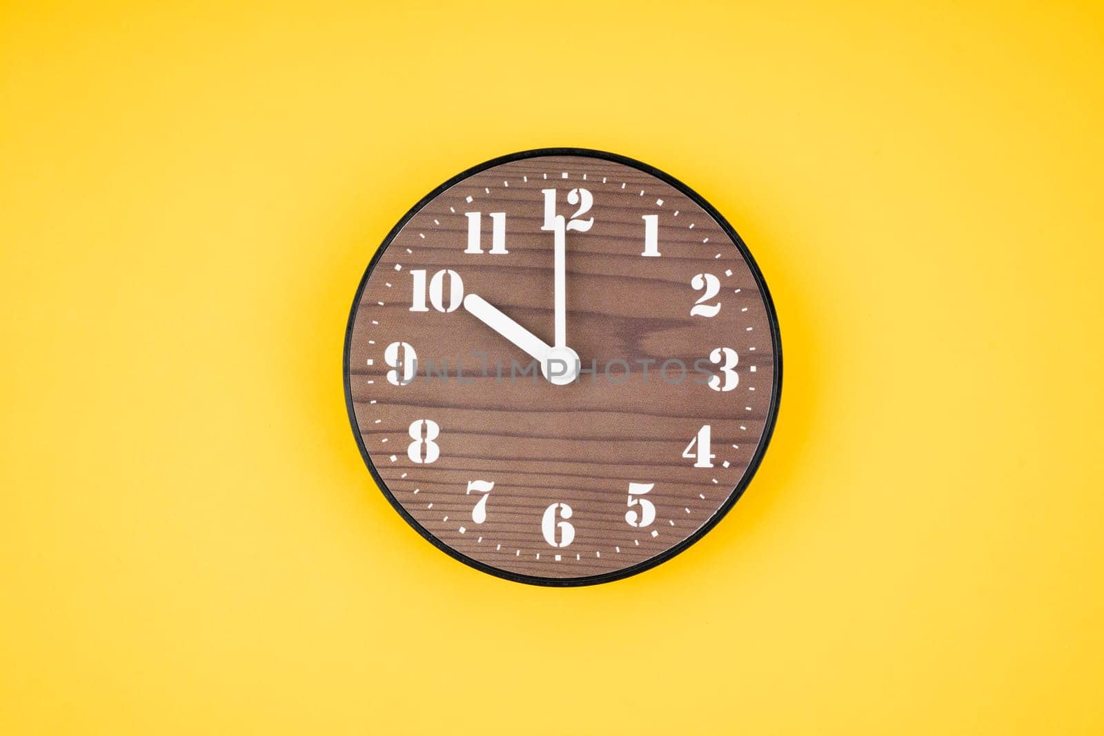 Retro wooden clock at 10 O' clock on yellow color background.