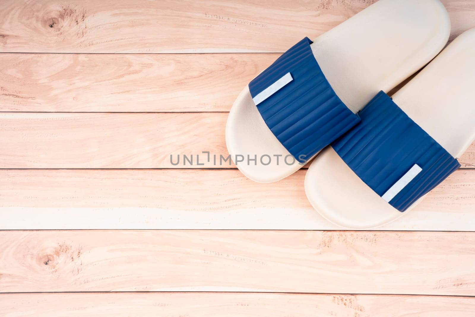 Top view of white and blue color rubber slipper shoes on wooden floor with copy space. Summer holiday vacation concept. by Gamjai