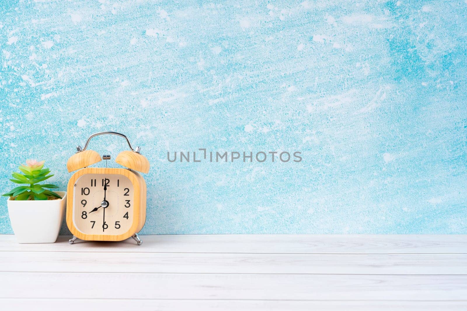 Wooden alarm clock and plant pot on blue wooden floor with copy space for your design.