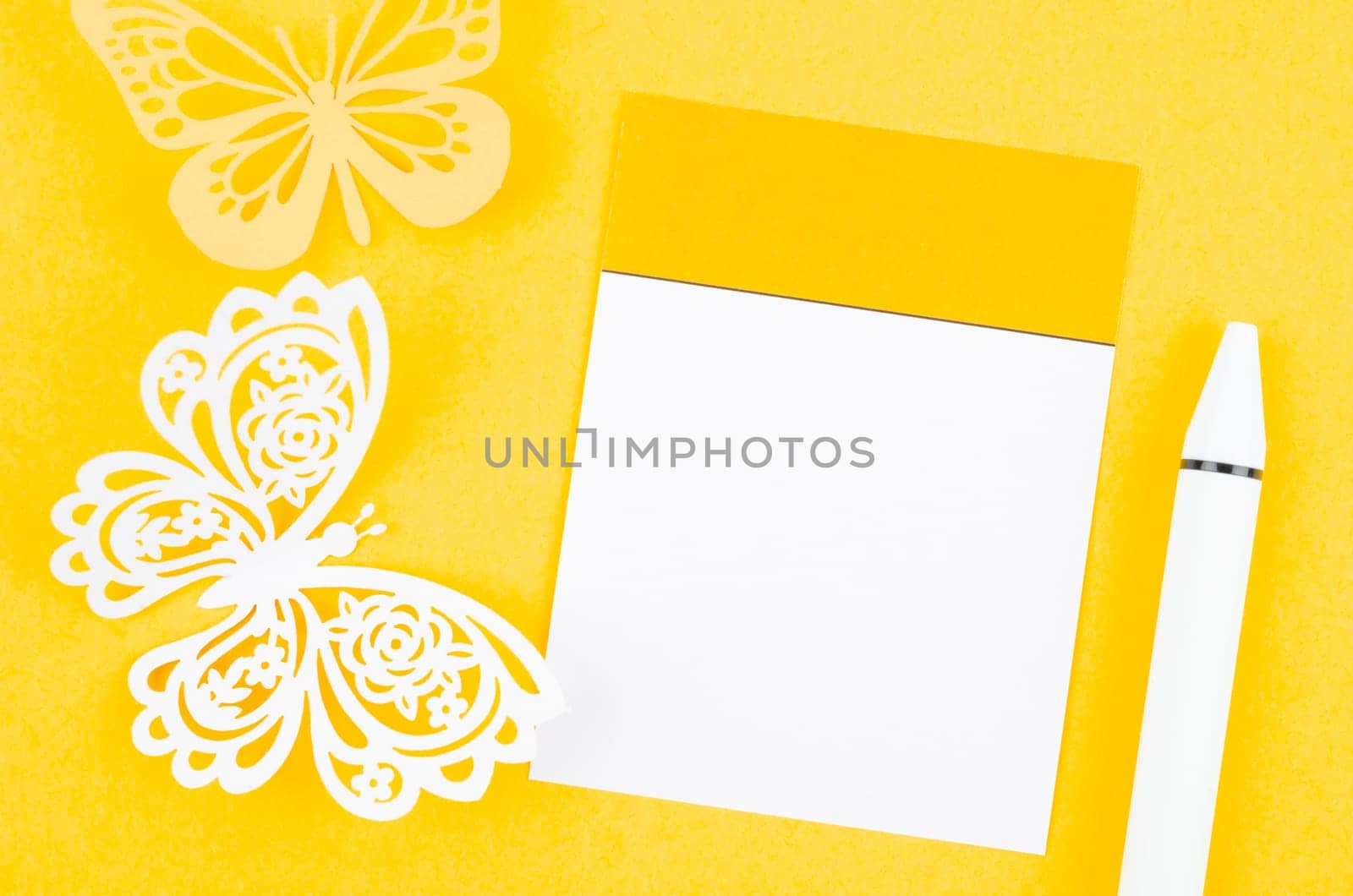 Blank paper note for reminder and carve of paper butterfly with the pen on yellow background, space for text.
