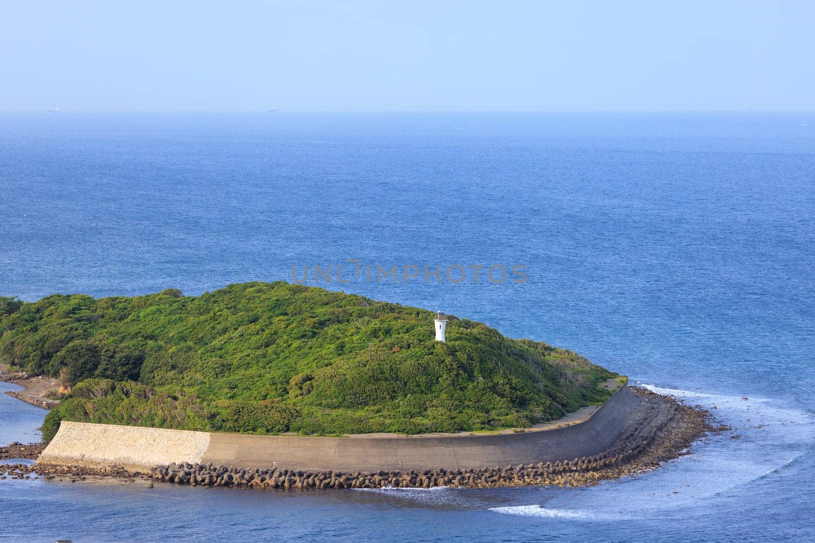 Concrete sea wall protects coastline on small green island with lighthouse. High quality photo