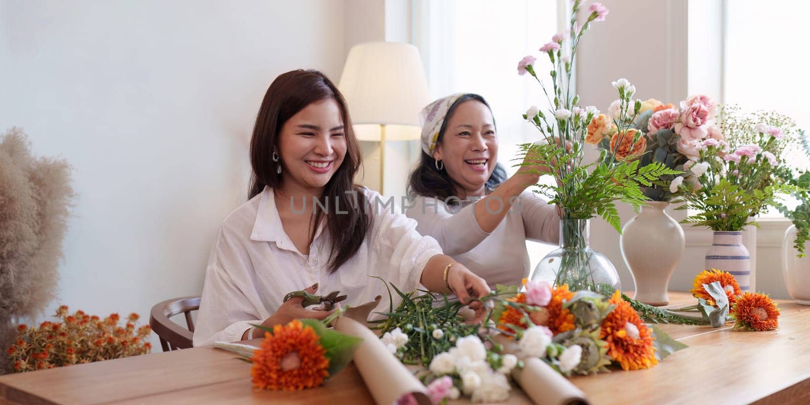 Startup, small business, flower shop. Young and older woman florist putting a flower on a vase.