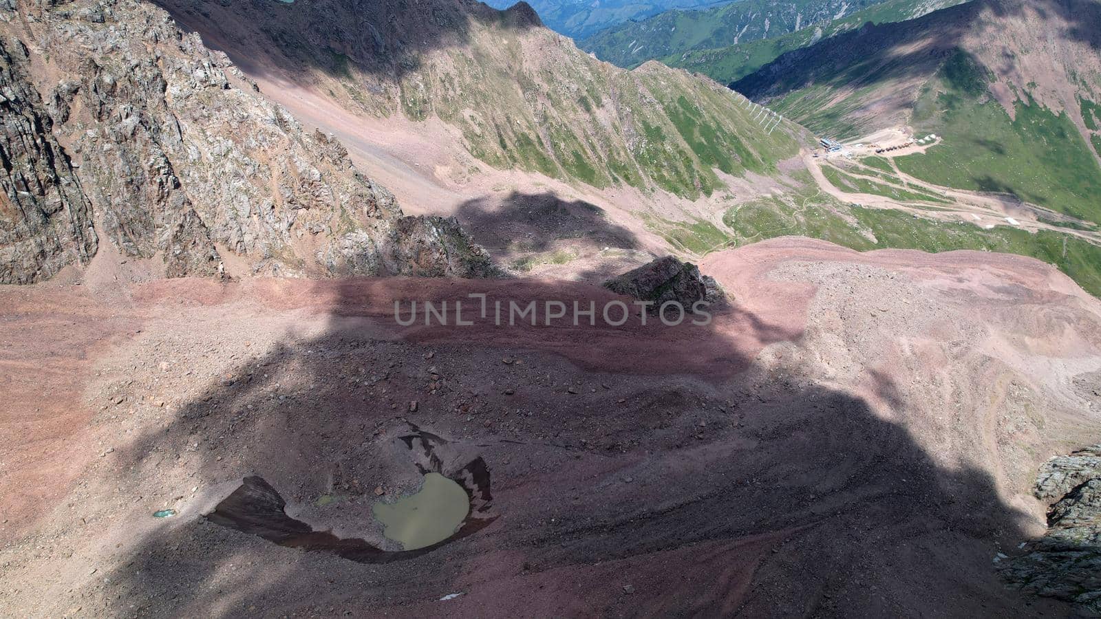 A moraine lake among a glacier covered with rocks. The glacier is melting. Shadows from clouds. View of the lake from above from the throne. A lake among high snowy mountains. Kazakhstan, Almaty