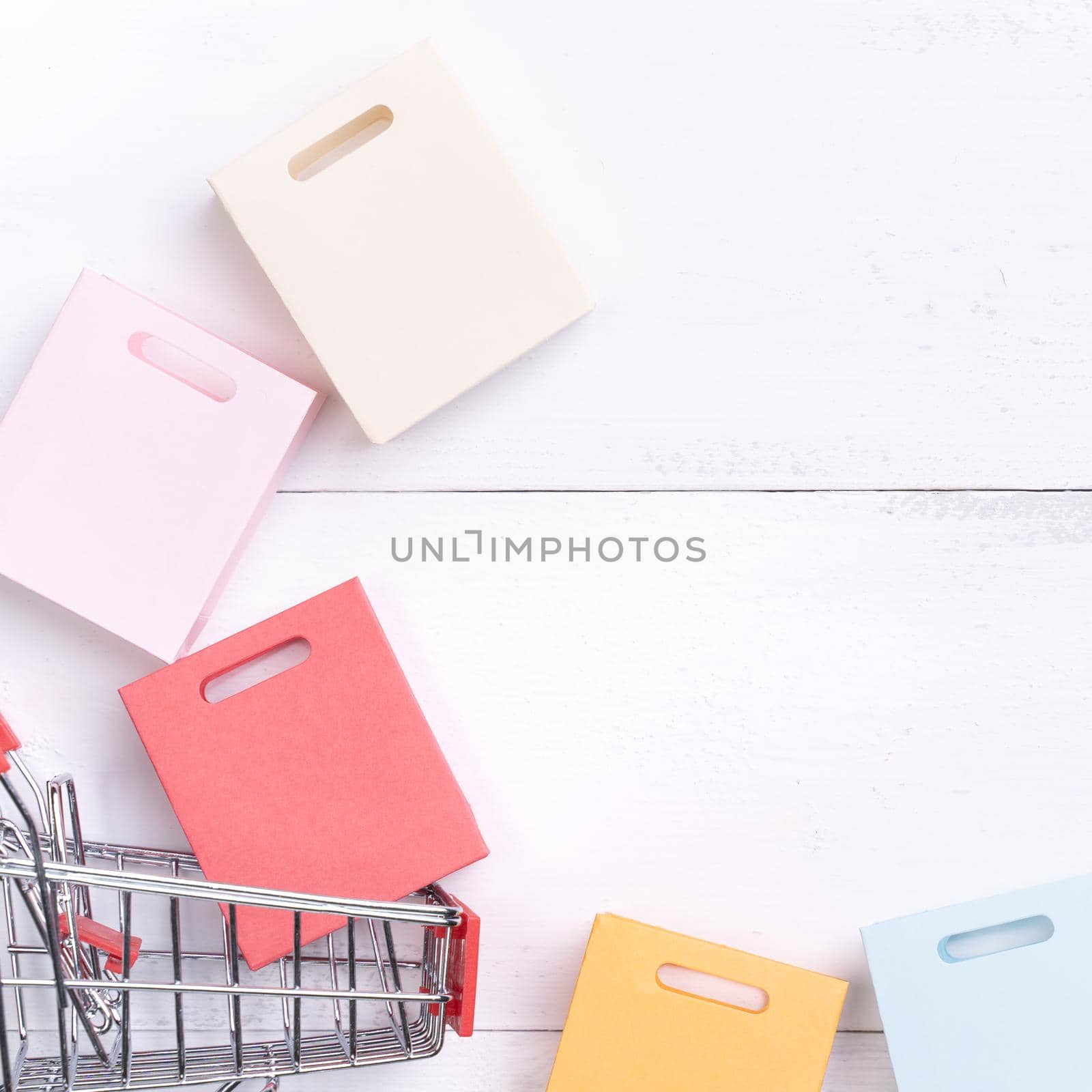 Abstract design element, annual sale, shopping season concept, mini cart with colorful paper bag on white wooden table background, top view, flat lay