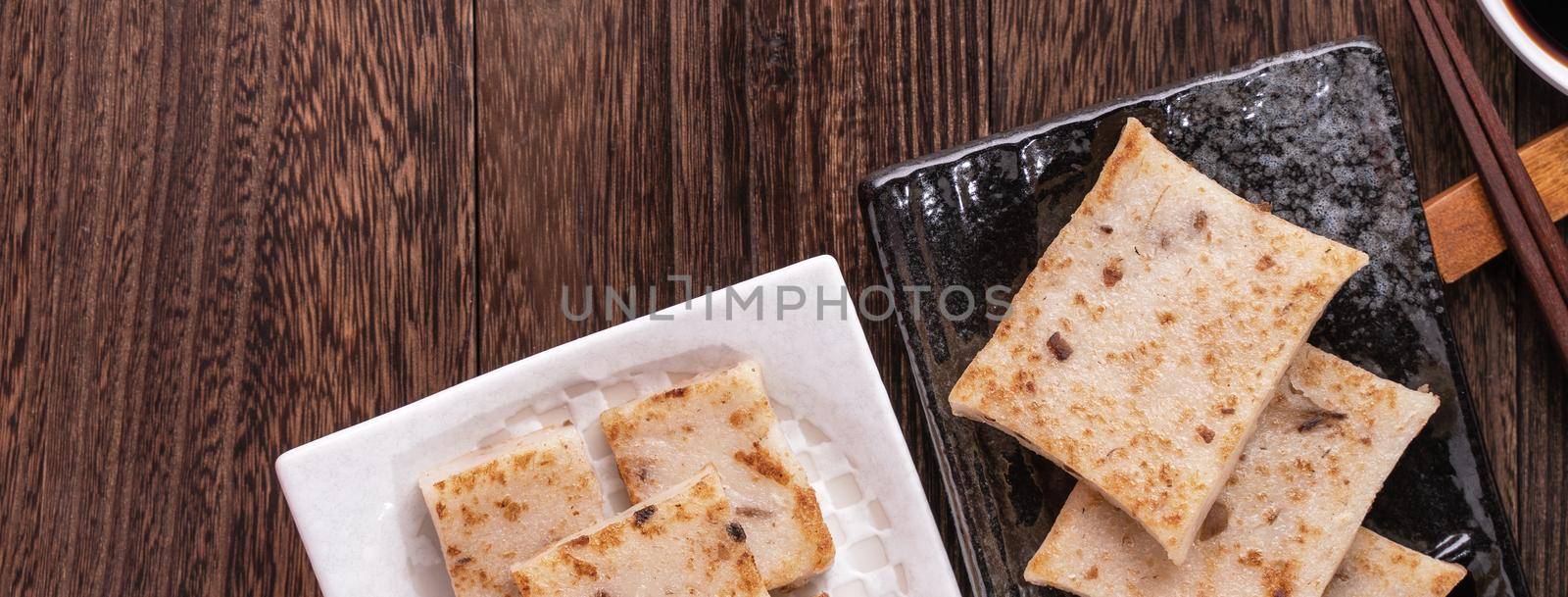 Delicious turnip cake, Chinese traditional local radish cake in restaurant with soy sauce and chopsticks, close up, copy space, top view, flat lay. by ROMIXIMAGE