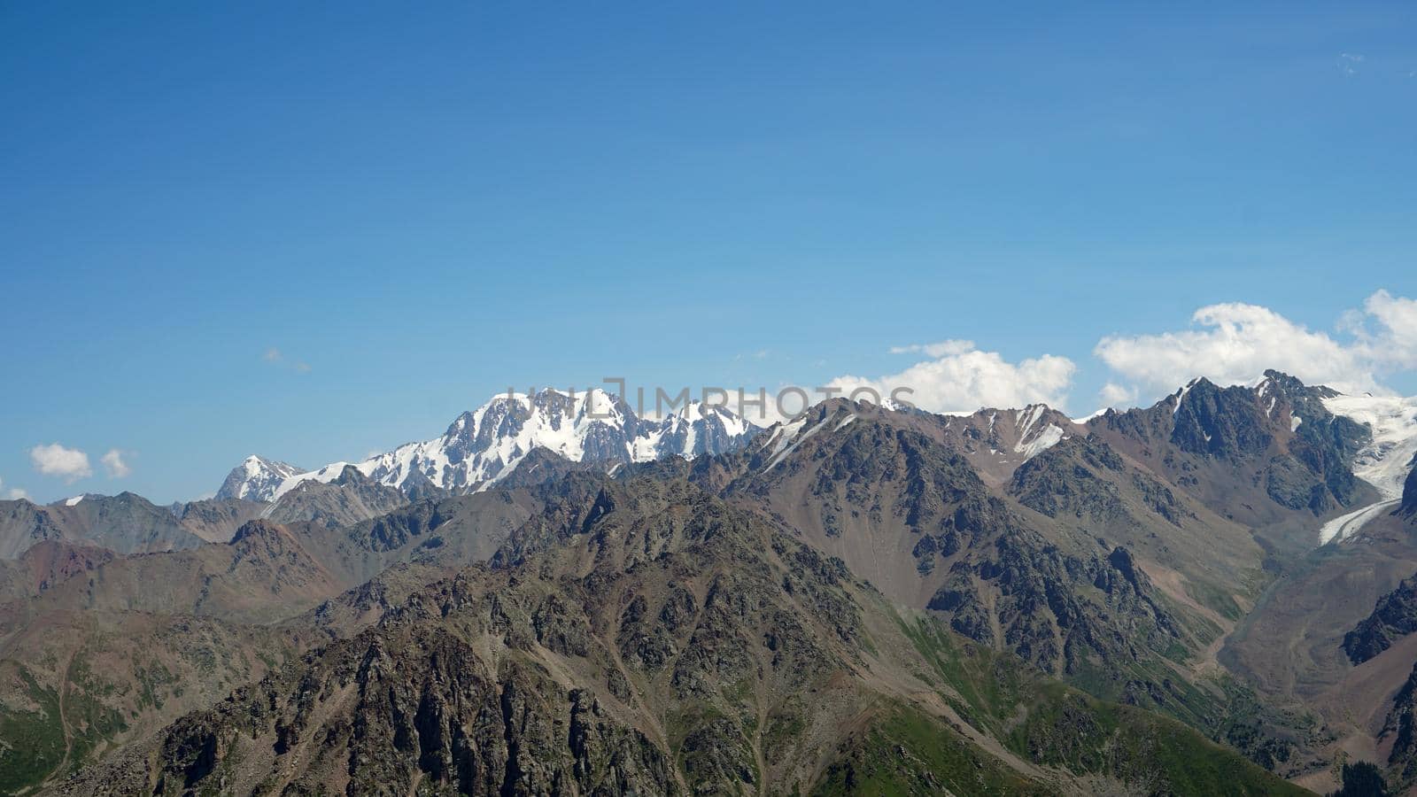 High mountains covered with snow in places. Green grass grows. Huge rocks and cliffs. In the distance, you can see peak of Talgar and Nursultan. A rocky gorge. Rowing peaks from a height. Kazakhstan