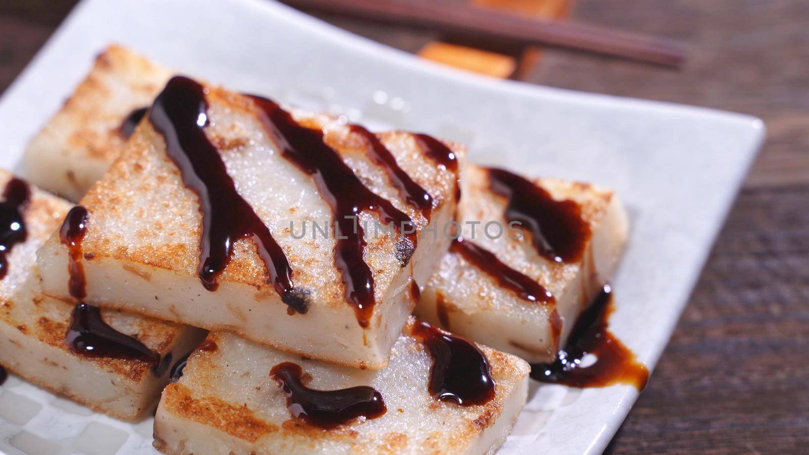 Pouring black soy sauce on ready-to-eat delicious turnip cake, Chinese traditional local dish radish cake in restaurant, close up, copy space.