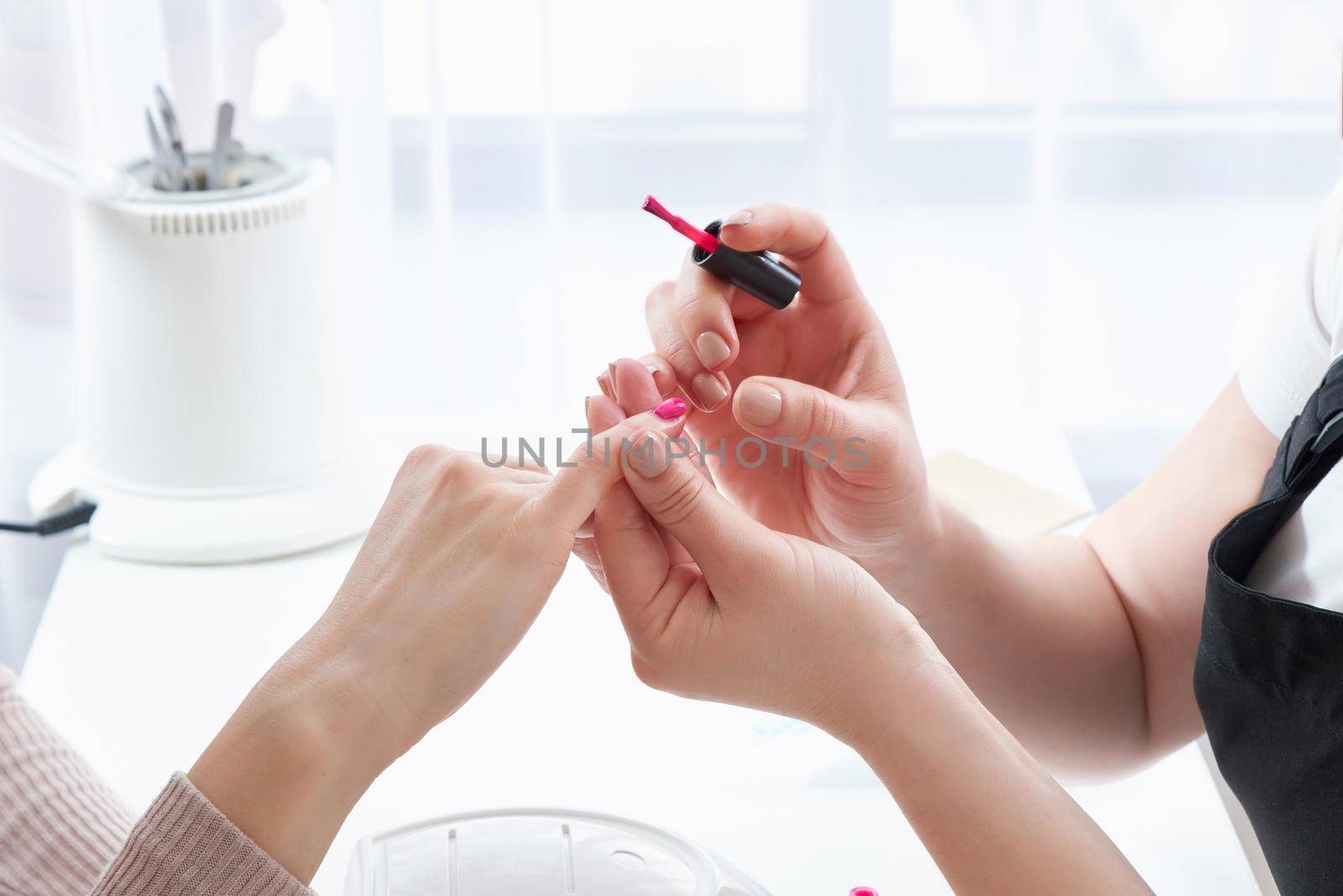 woman in a nail salon receiving a manicure by a beautician with nail file. Woman getting nail manicure. Beautician file nails to a customer.
