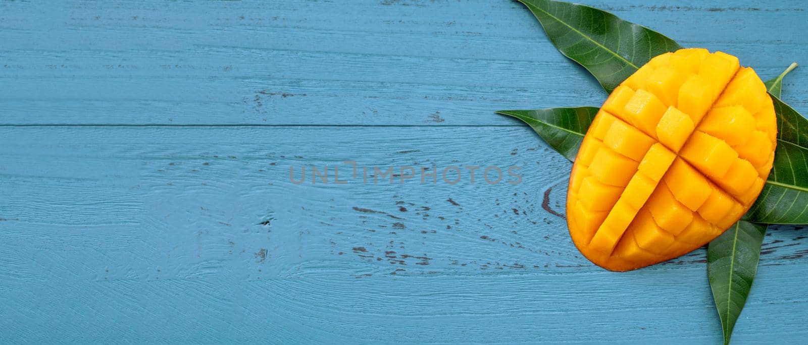 Fresh mango - beautiful chopped fruit with green leaves on dark blue timber background. Tropical fruit design concept. Flat lay. Top view. Copy space by ROMIXIMAGE
