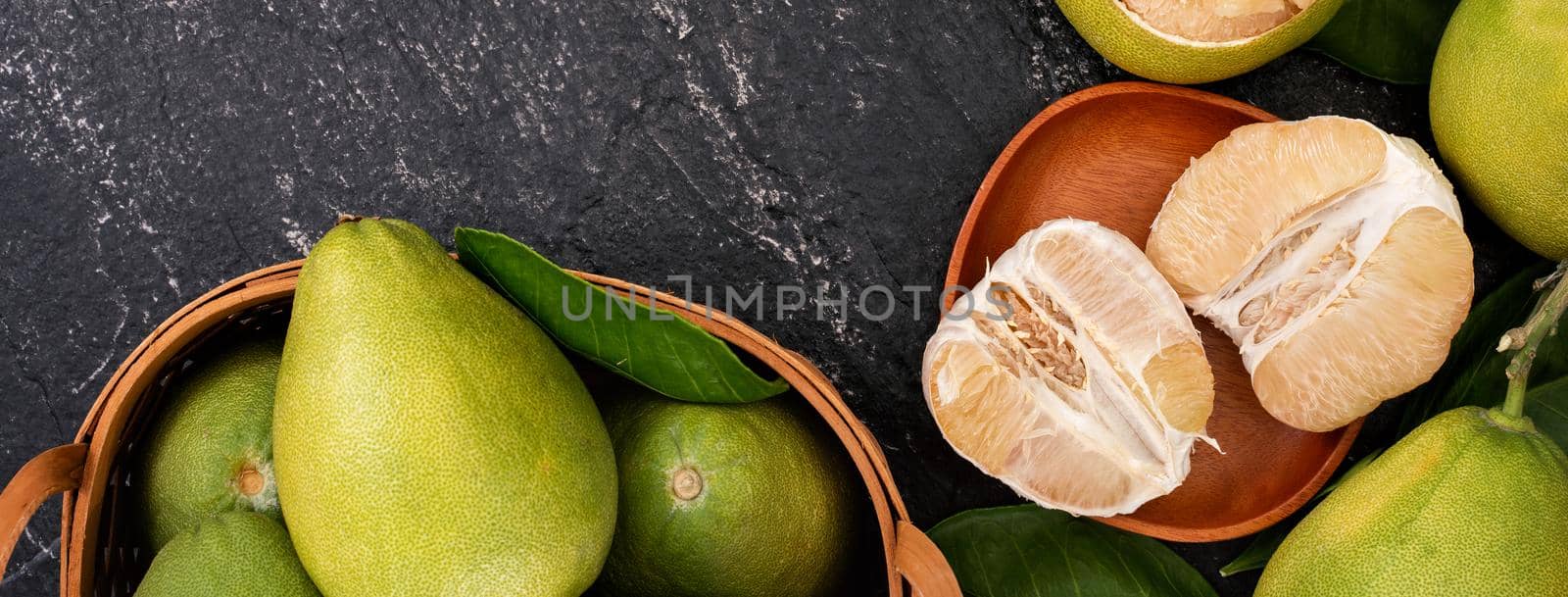Fresh pomelo,grapefruit in bamboo basket with green leaf on dark black slate background. Seasonal fruit for Mid-Autumn Festival. Top view. Flat lay. by ROMIXIMAGE