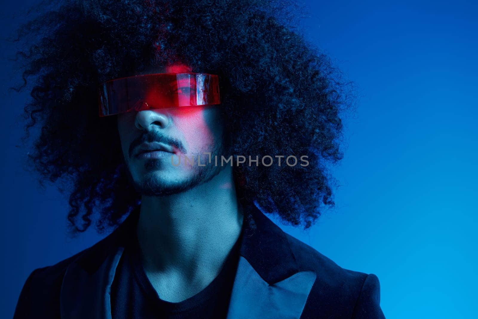 Fashion portrait of a man with curly hair on a blue background wearing red sunglasses, multinational, colored light, trendy, modern concept. High quality photo