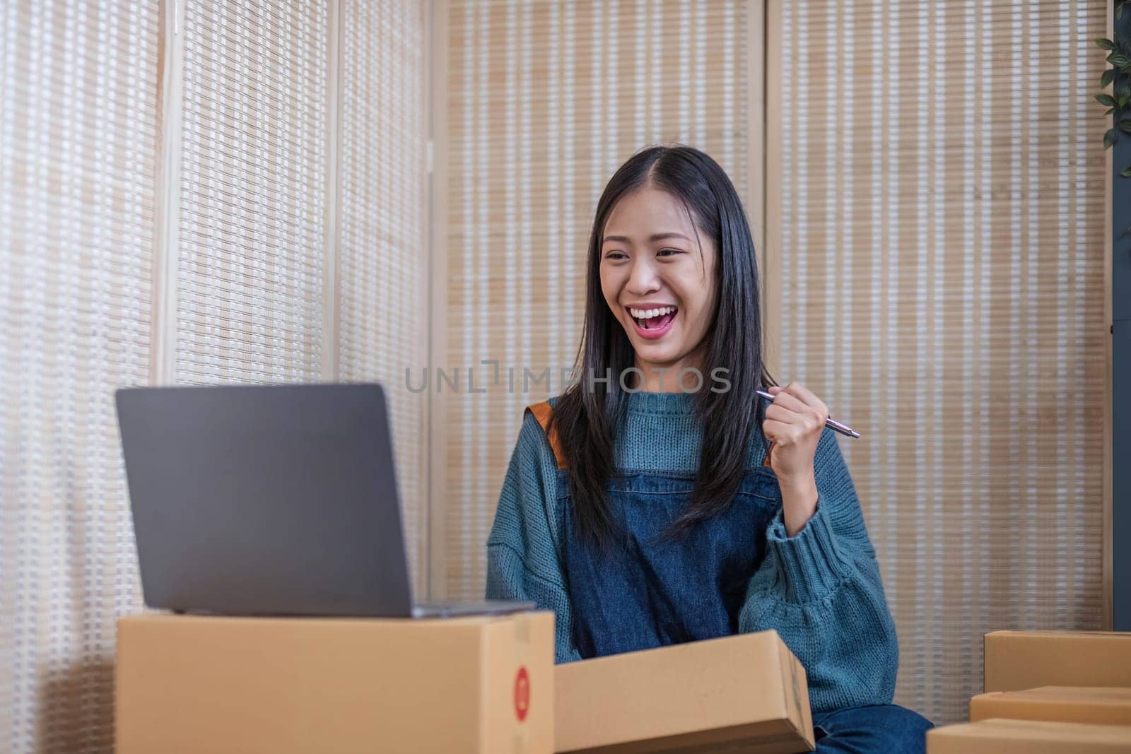 Happy young Asian woman entrepreneur, Smile for sales success after checking order from online shopping store in a laptop at home office, Concept of merchant business online and eCommerce..