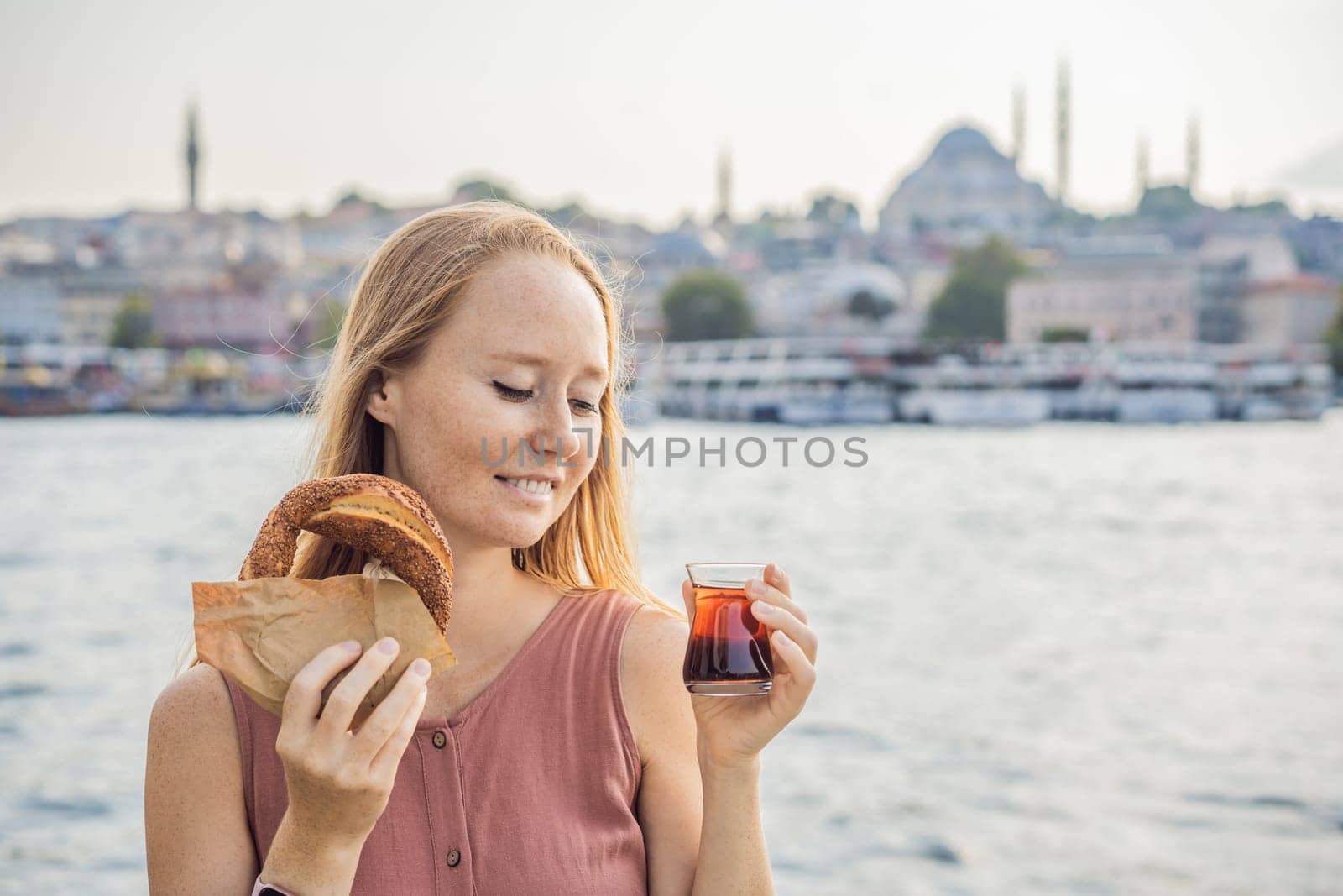 Woman in Istanbul having breakfast with Simit and a glass of Turkish tea. Glass of Turkish tea and bagel Simit against golden horn bay in Istanbul, Turkey. Turkiye.