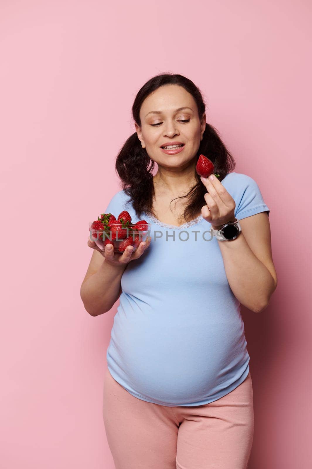 Pregnant vegetarian woman eats fresh tasty sweet strawberries. Organic nutrition and balanced diet for expectant mother by artgf