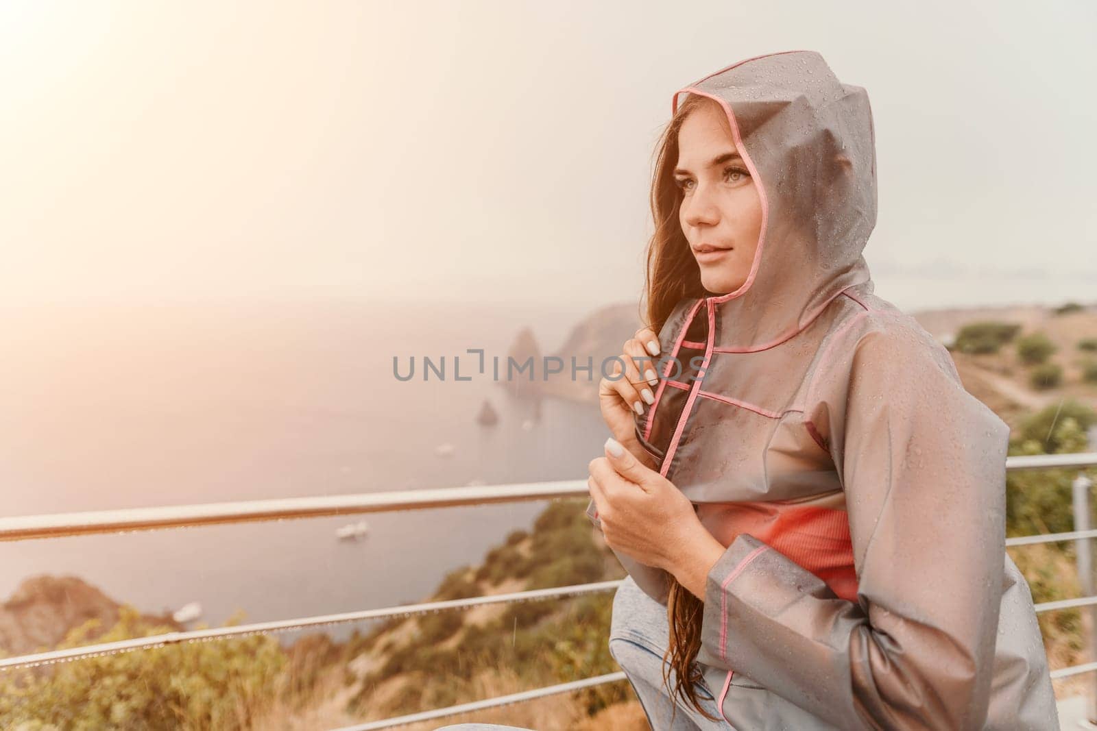 Woman rain park. Happy woman portrait wearing a raincoat with transparent umbrella outdoors on rainy day in park near sea. Girl on the nature on rainy overcast day