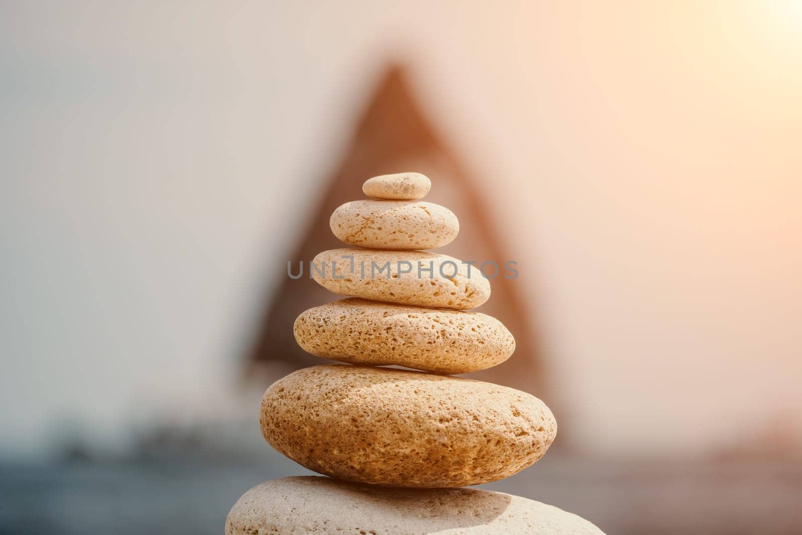 Pyramid stones on the seashore with warm sunset on the sea background. Happy holidays. Pebble beach, calm sea, travel destination. Concept of happy vacation on the sea, meditation, spa, calmness.