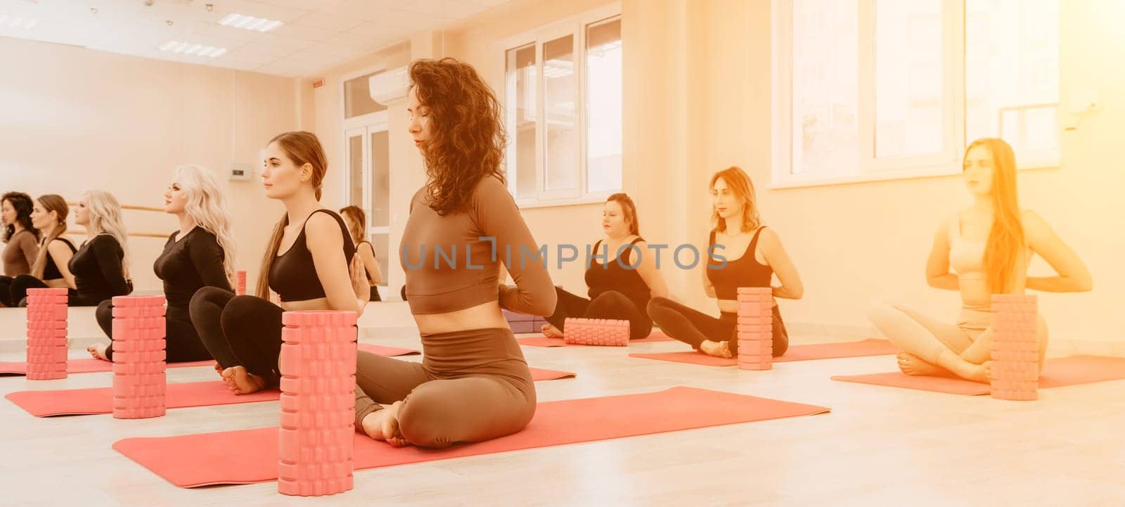 Group of young womans fitness instructor in Sportswear Leggings and Tops, stretching in the gym before pilates, on a yoga mat near the large window on a sunny day, female fitness yoga routine concept.