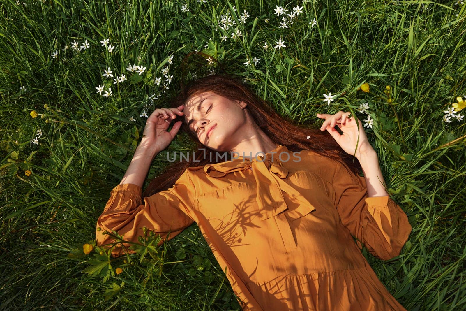 a relaxed woman, resting lying in the green grass, in a long orange dress, with her eyes closed and a pleasant smile on her face, recuperating. High quality photo