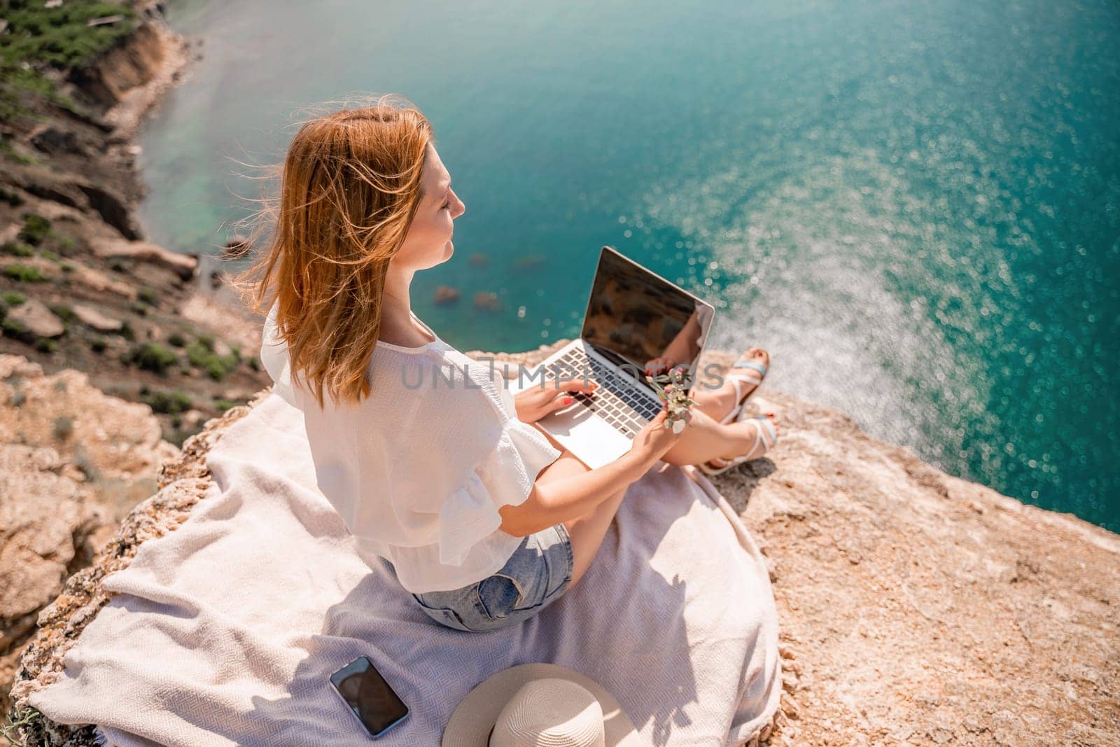 Freelance woman working on a laptop by the sea, typing away on the keyboard while enjoying the beautiful view, highlighting the idea of remote work