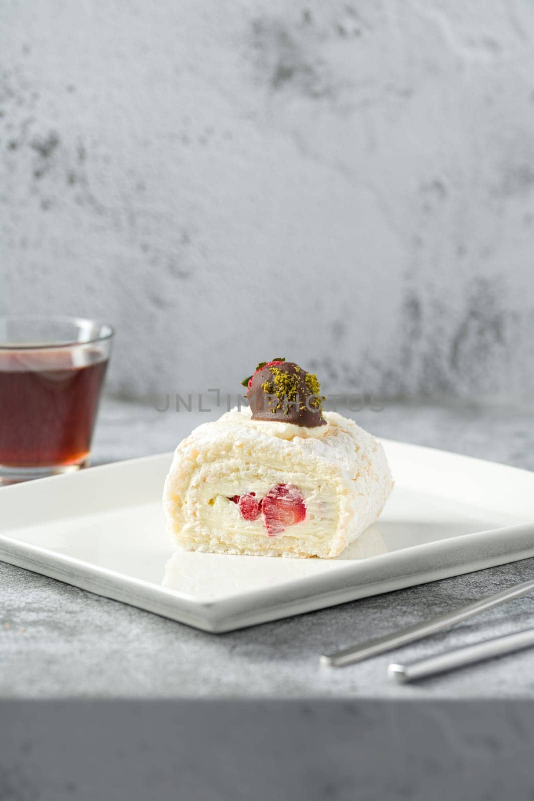 Strawberry roll cake with tea next to it on stone table by Sonat