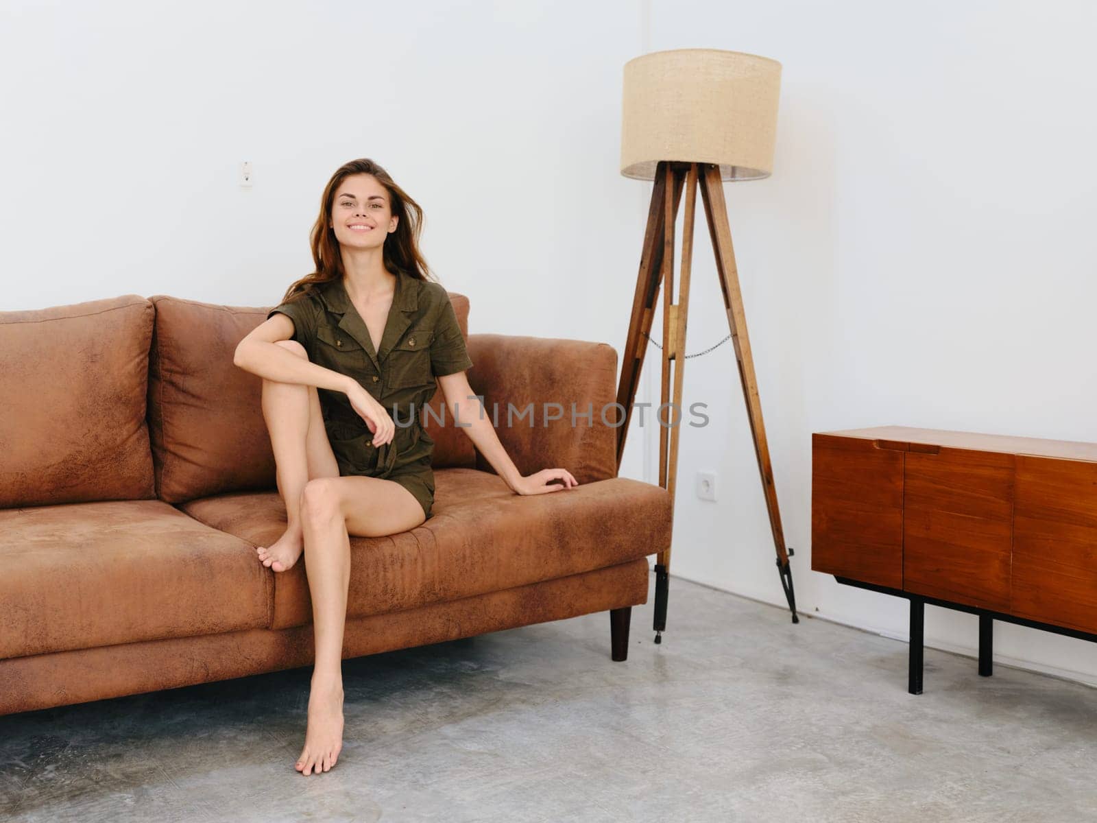 Young woman model sitting on the couch at home smiling and relaxing, modern interior lifestyle, copy space. by SHOTPRIME