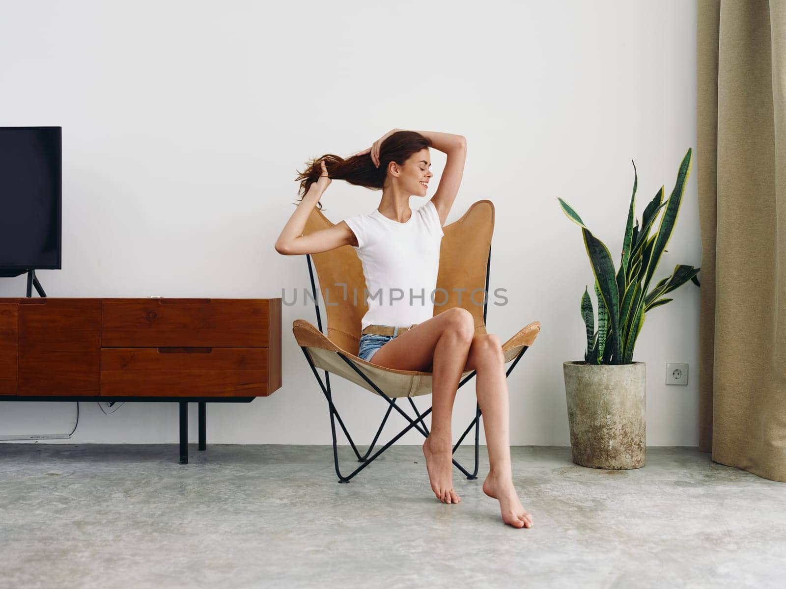 Woman sitting in leather armchair smile with teeth Lifestyle, relaxing at home stylish modern interior with white walls, copy space. by SHOTPRIME