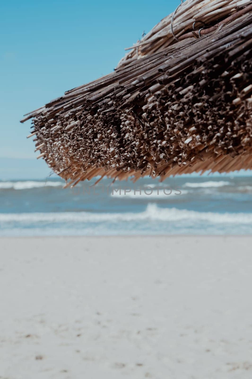 Straw beach rattan parasol at the empty beach with blue sky backgrounds sea ocean coast. Relaxing day. Copy space for your text. Idyllic travel and summer vacation concept. Straw umbrella on beautiful tropical beach.