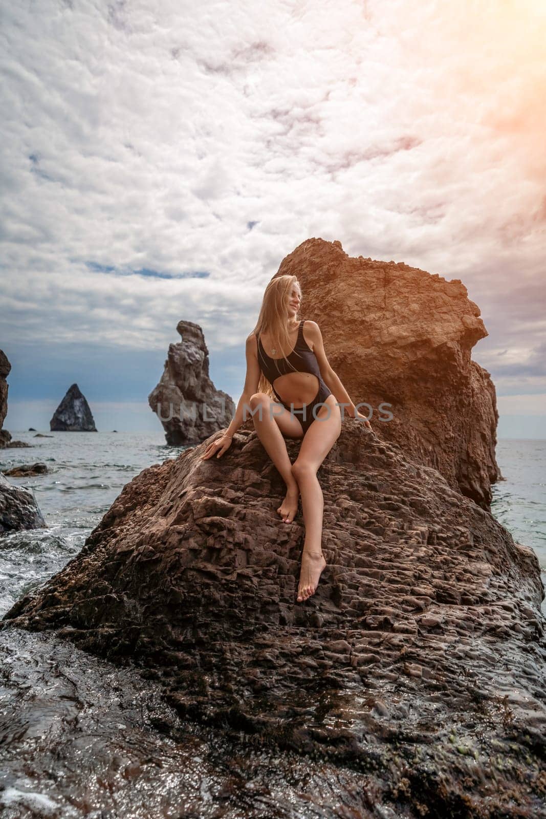 Woman swimsuit sea. Attractive blonde woman in a black swimsuit enjoying the sea air on the seashore around the rocks. Travel and vacation concept. by Matiunina