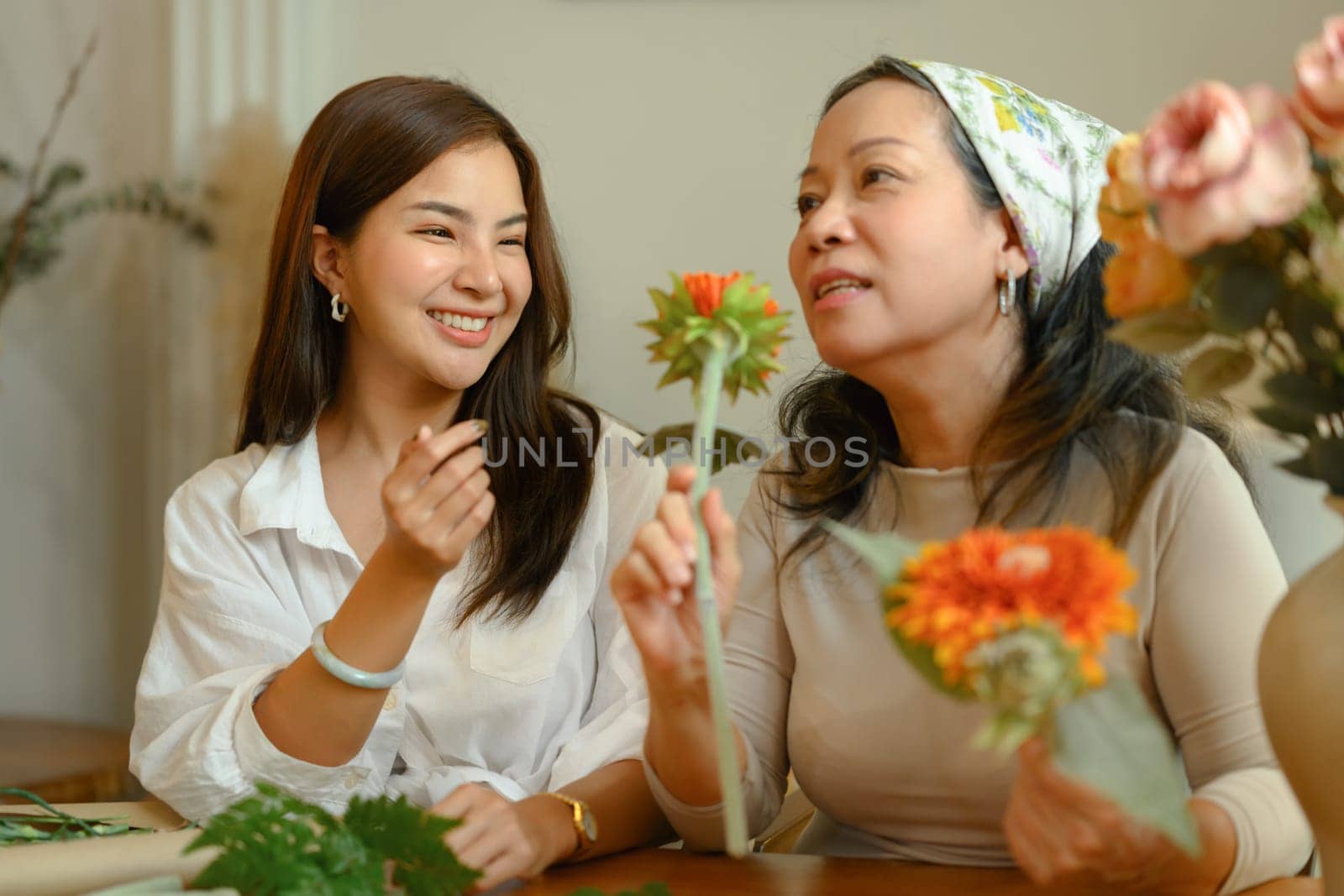 Happy young asian woman and senior mother making a bouquet with fresh flowers at floral shop. Small business concept.