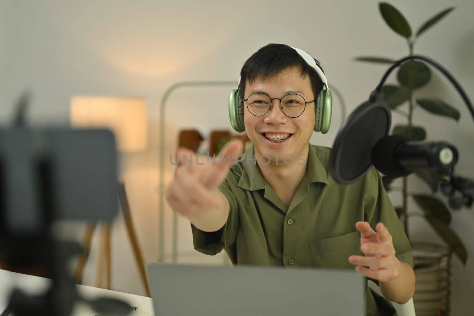 Cheerful man radio host in headphone using condenser microphone to recording podcast in small home studio.