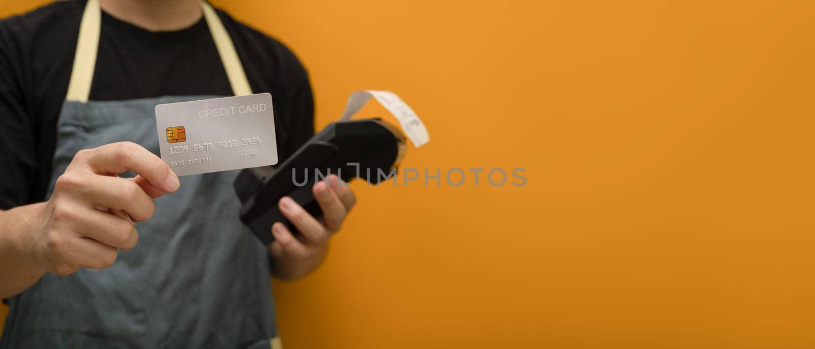 Unrecognizable holding credit card and payment terminal on yellow background. Electronic money, contactless payment concept.