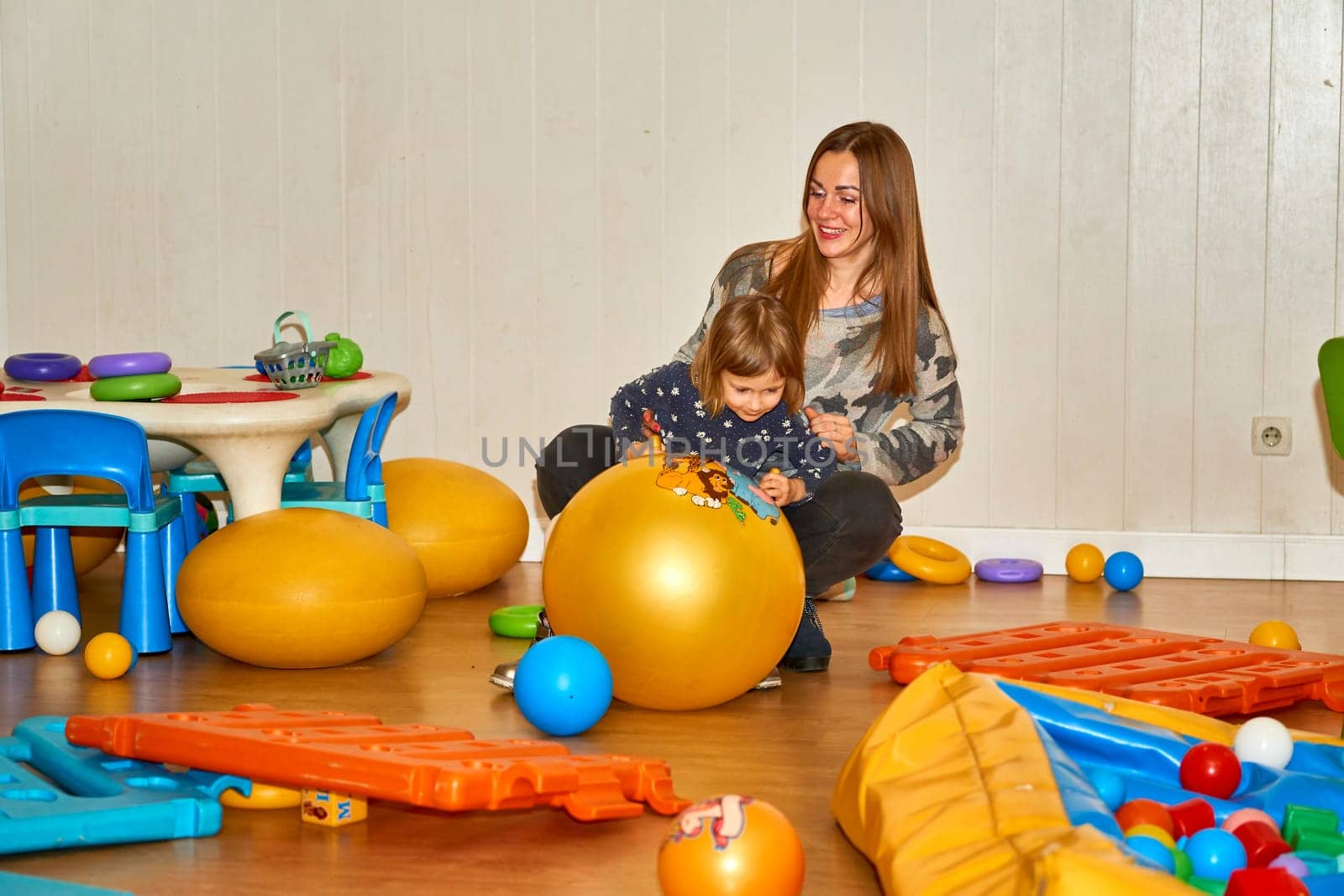 Pretty mother playing with cute daughter baby girl in playroom in kindergarten by jovani68