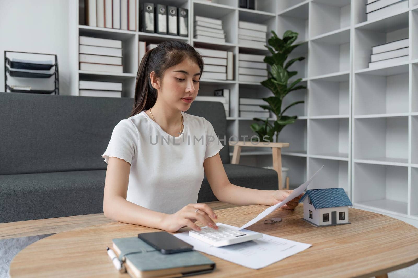 Young woman sit at desk at home manage household finances paying bills calculating on machine calculator. female care of budget use smartphone for payment. Finance concept.