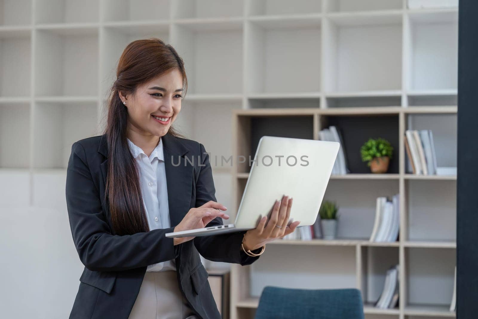 Young smart business woman , female company worker or manager holding laptop using technology device working standing in modern corporate office.
